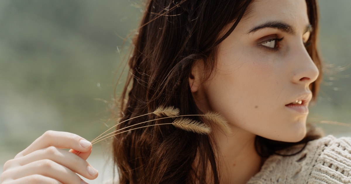 An image of a close up of a young woman with long brown hair and fair skin, looking off to the side